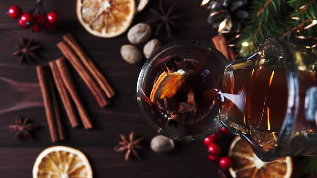 Shooting from above mulled wine is poured into a glass mug with a slice of orange, cinnamon stick and anise