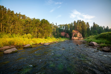 water stream in river of Amata in Latvia with sandstone cliffs, green foliage