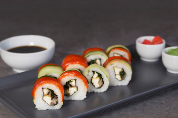 Sushi rolls on grey plate, wasabi, pickled ginger, soy sauce on gray background. Culinary, menu, asian food concept. Close-up, copy space, layout design