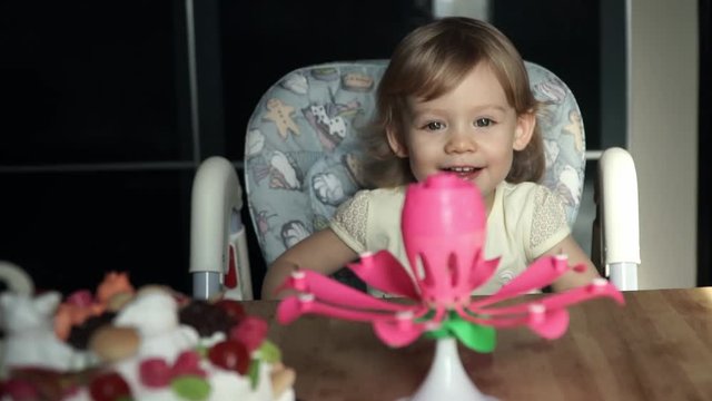 Little cute girl with big blue beautiful eyes is sitting in front of a festive cake and candles and smiling