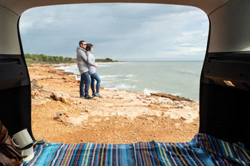 Joven pareja abrazándose mientras miran el mar Mediterráneo en un soleado día de invierno,...