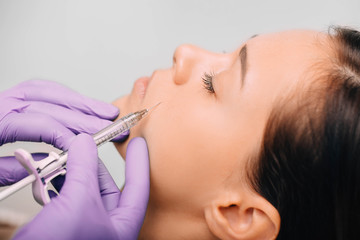 Beautiful woman having facial injection into area near mouth and nose. Anti age collagen injections into face. Beautician making injections for facelift.