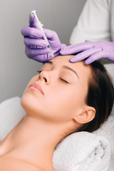 Obraz na płótnie Canvas Beautiful woman having facial injection into forehead. Anti age collagen injections into face. Remove wrinkles on forehead ,facelift.
