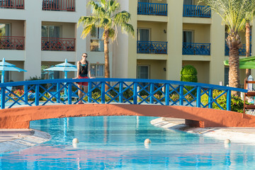 Young woman on the bridge over the pool against the background of the hotel