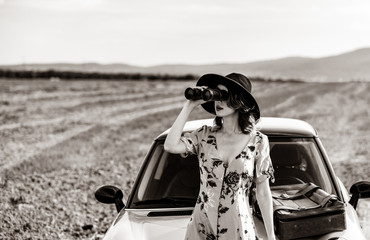 Portrait of young woman in dress with map and suitcase near a yellow car at autumn countryside. Image in black and white color style