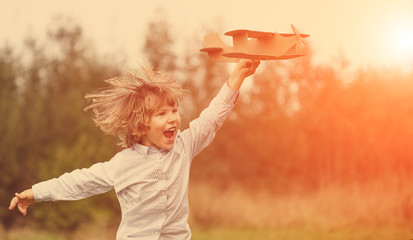 Child pilot aviator with plane at sunset, little boy playing with cardboard toy airplane outdoors, against summer sky background. Retro toned. dreams of traveling © Miramiska