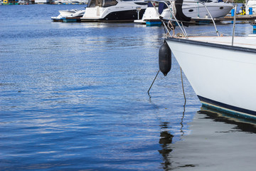 Black color fender hangs on the nose of a white white yacht. Blue water. Part of the frame