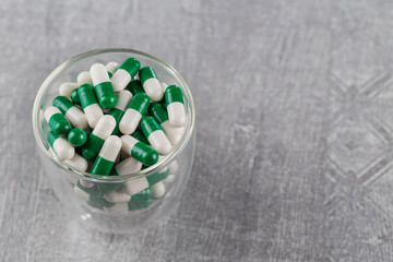 close-up of white-green pills in glass Cup on grey background