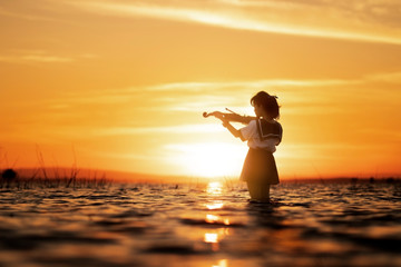 Girl playing violin on water with sunset background