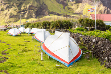 Countryside grass street with a row of drying overturned boats. British Governor flag flying....