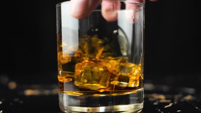 Man hand hold glass with whiskey on gold marble surface in slow motion.