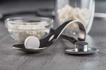 close-up of a large white tablet on a metal spoon on background a stethoscope and medication