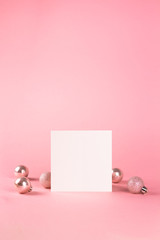Obraz premium Mock up with square invitation card on trendy pastel light pink background with christmas ornaments. Greeting card and silver Christmas baubles. Minimal christmas concept.