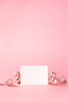 Mock up with horisontal invitation card on trendy pastel light pink background with christmas ornaments. Greeting card and silver Christmas baubles. Place for text