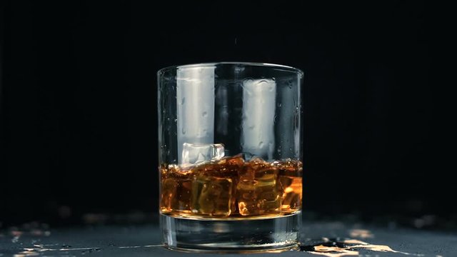 Ice cubes falling in glass of whiskey with splash in slow motion. Close up.