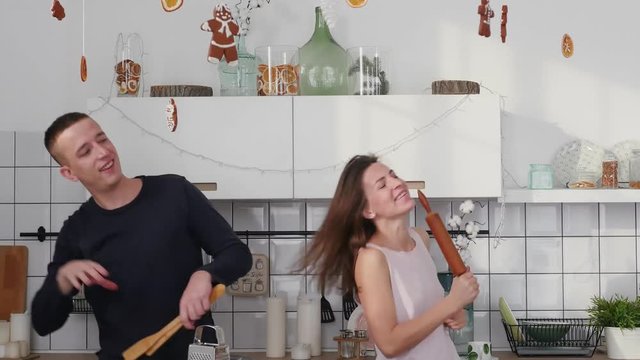 Young joyful couple have fun dancing and singing while cooking in the kitchen at home