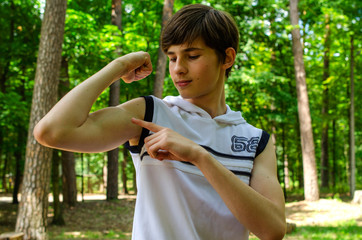 Teenager boy in a white sports shirt without a sleeves shows biceps on his hands