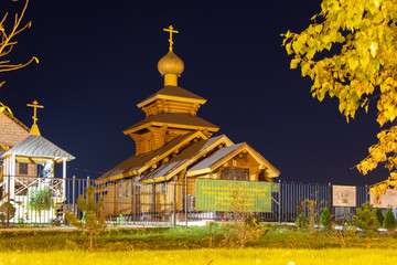 Wooden small church made of logs. Metallic fence. green grass, night sky. Translation of the text...