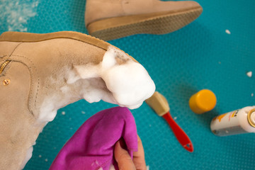 Closeup of the process of caring for suede shoes. A woman cleans suede boots with a special cleansing foam, brush and microfibre cloth. Restoration of suede shoes
