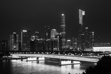Black and white photography. Night modern city with skyscrapers. Bridge over the river, city buildings glow at night.