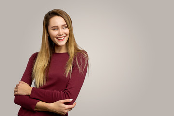 European woman keeps hands pressed together, looks with happy expression aside, has toothy smile, isolated over white background. People and emotions concept