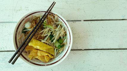 Dry noodles Crispy wonton with  Wooden Chopsticks on bowl Placed on a white wood table.