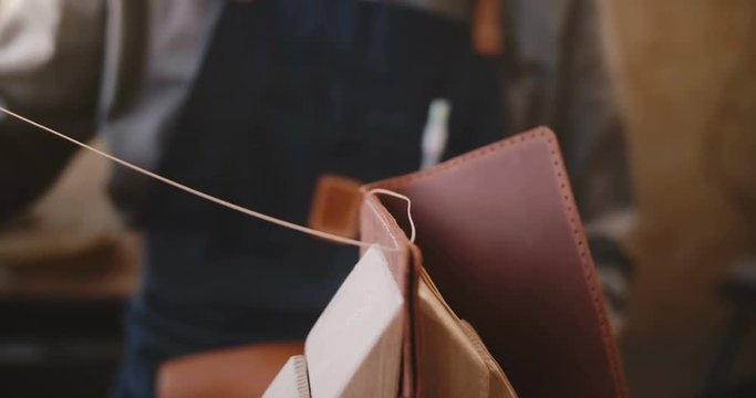 Close-up shot of professional artisan businessman hands sewing handmade leather bag on saddler in a manufacture workshop