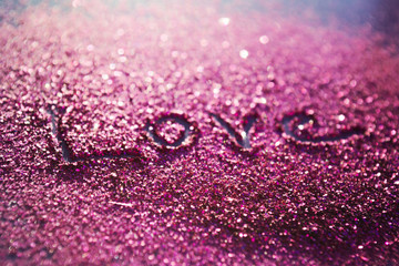 The word love written in pink glitter sand