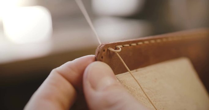 Macro close-up shot of leather sewing process details, hands with needle and strings making a bag on saddler in workshop