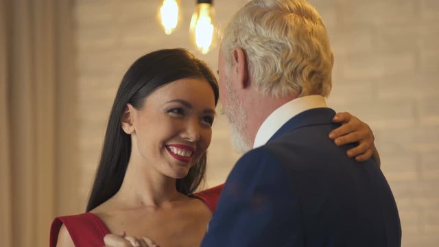 Young woman flirting and dancing with old millionaire on date, escort service