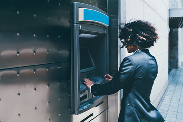 Side view of a businessman withdrawing money from his bank card using an outdoor ATM;  a curly man...