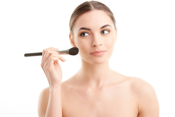 Young naked woman applying makeup. Studio shot.