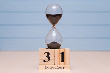 December 31st set on wooden calendar and hourglass with blue background.