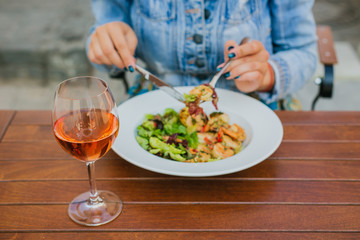Girl, eating salad with shrimps, drinking a glass of rose wine