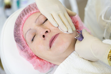 Fototapeta na wymiar Cosmetologist making injection in face of senior woman. Skin aging, rejuvenation, face lifting procedures. Aged woman gets beauty facial injections in cosmetology clinic.
