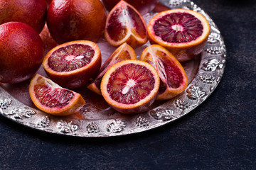 Whole and sliced sicilian oranges on a black slate background.