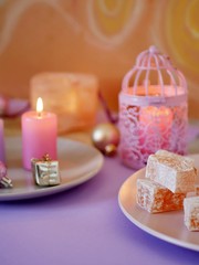 Decorative composition in a pink color from burning candles, decorative lanterns, oriental sweets on dishes, Christmas decor, balls on a light silver background, romantic atmosphere, seasonal winter h