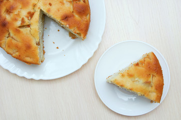 Sliced piece of cake on a white plate. Pie on the kitchen table.