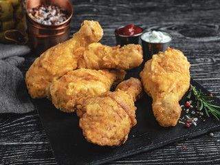 fried chicken leg in batter, red and white sauce on a dark surface