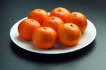 ripe tangerines in a white plate on a black background