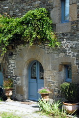 Ville de Genêts, porte et fenêtres bleues, glycine monte le long du mur en granit, département de la Manche, France