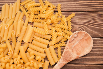 pasta of different types taken from the top and wooden spoon. Food background concept.