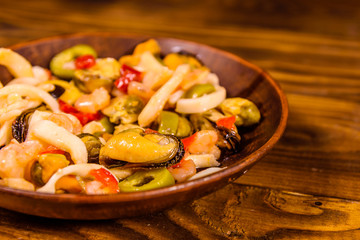 Ceramic plate with different sea food and olives on wooden table