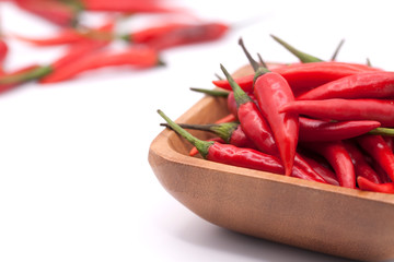 Red chili peppers in a wooden bowl. Isolated on white background. Next to a scattered pile of...