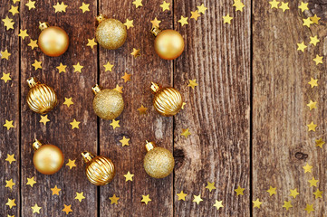 Shiny Christmas background in warm colors 2019: Golden balls and star confetti on wooden rustic table.