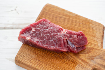 Morning in the kitchen. Raw meat. Raw fresh beef steak on a wood cutting board. White wooden background, top view, copy space, Daylight