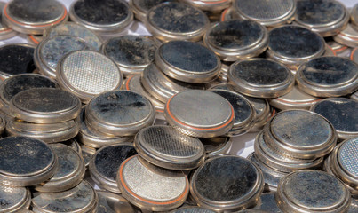A pile of button batteries to be recycled. The batteries are old and dirty, and are the type used in desktop computers. Focus is on the closer batteries.