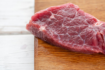 Morning in the kitchen. Raw meat. Raw fresh beef steak on a wood cutting board. White wooden background, top view, copy space, Daylight