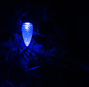 Blue light balb shaped as a pinecone among the pine leaves in the night dark.