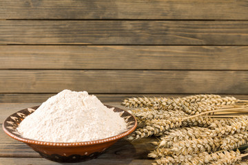 Wheat spikelets and flour on wooden plank background